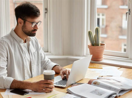 A man sitting at a desk with a laptop and a cactus.